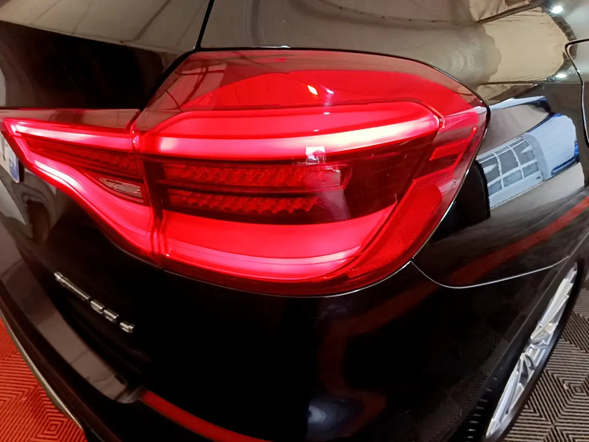 Gros plan sur le feu arrière droit rouge d’un BMW X3 noir, version xDrive20d, avec reflet du garage visible.
