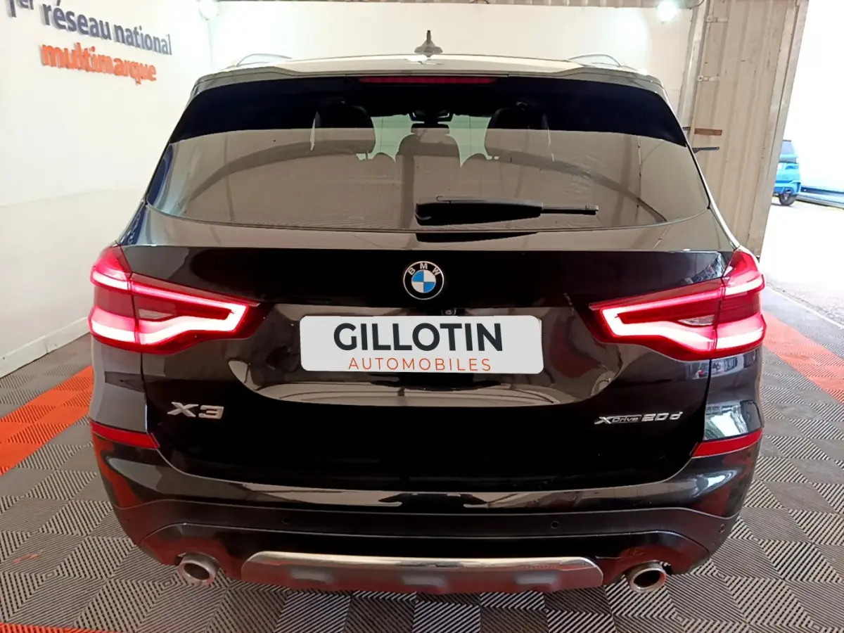 Vue arrière d'un BMW X3 noir avec feux LED allumés et double sortie d'échappement visible en intérieur showroom.