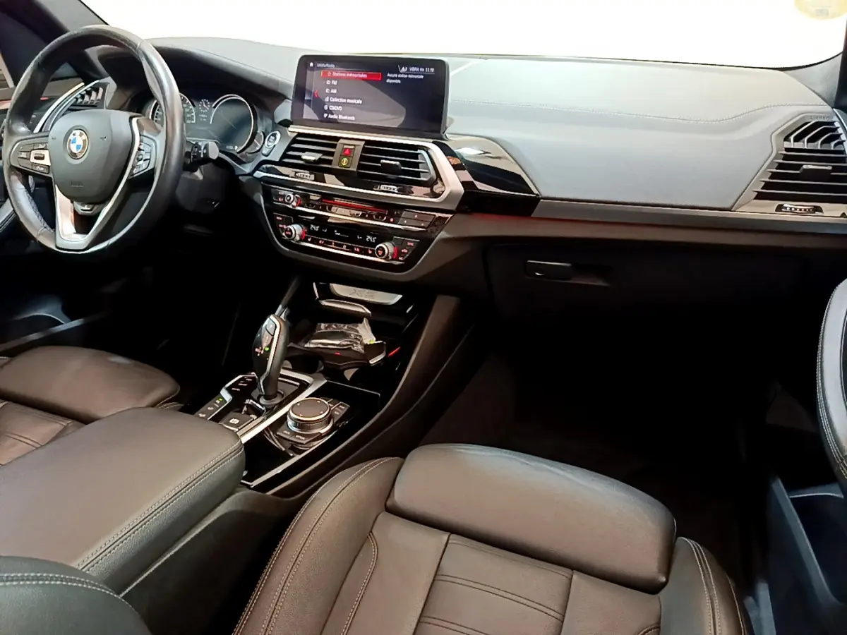 Vue intérieure du tableau de bord et console centrale du BMW X3 noir, avec écran tactile et volant cuir multifonctions.