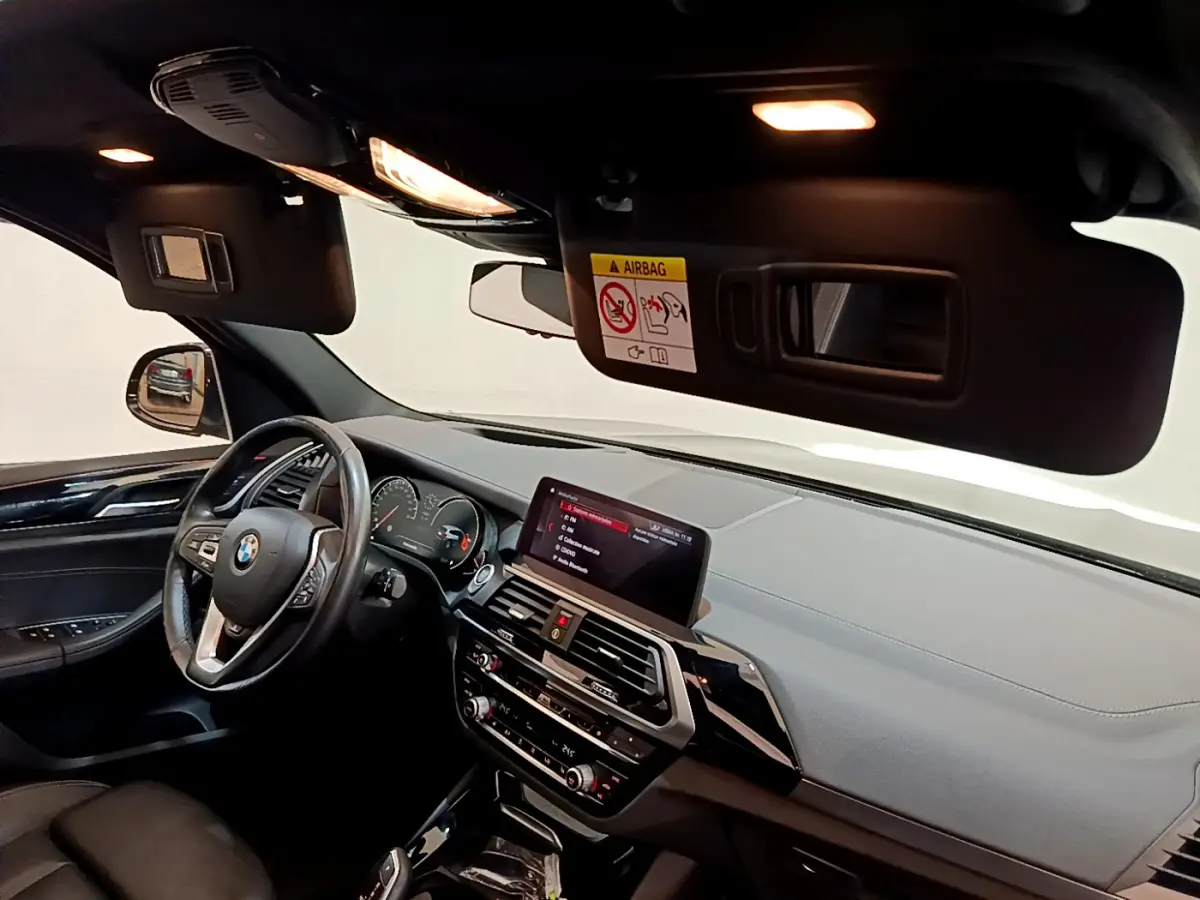 Vue intérieure avant gauche du BMW X3 noir de 2019, avec tableau de bord moderne et écran tactile central allumé.