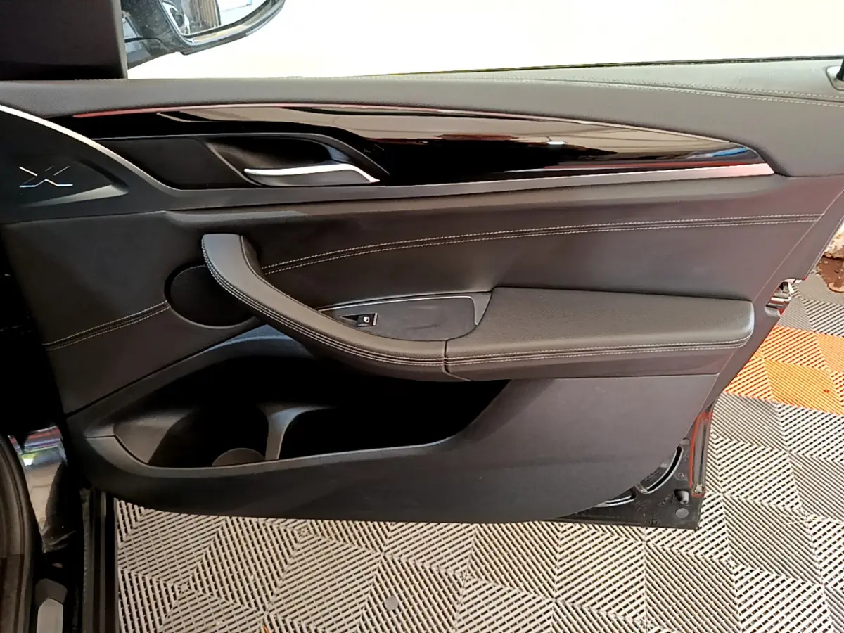Gros plan sur la porte intérieure côté gauche noire du BMW X3 2019 avec surpiqûres blanches et poignée intégrée.