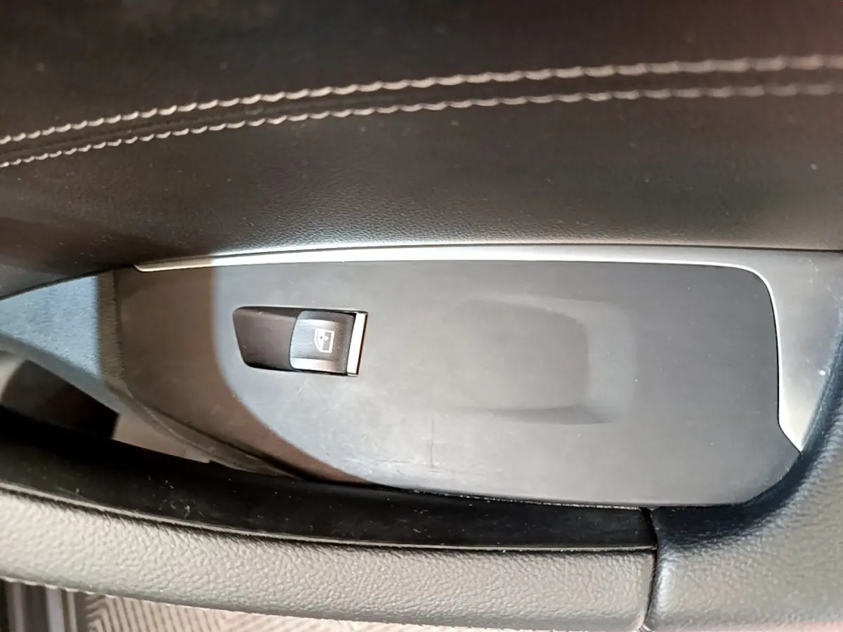 Gros plan sur le bouton de commande de la vitre électrique côté conducteur, entouré de garniture noire et coutures blanches.