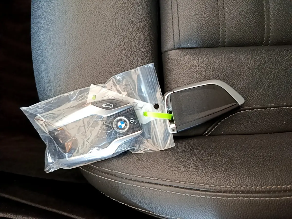 Clé BMW noire dans un sachet plastique posée sur un siège en cuir noir, vue rapprochée intérieure.