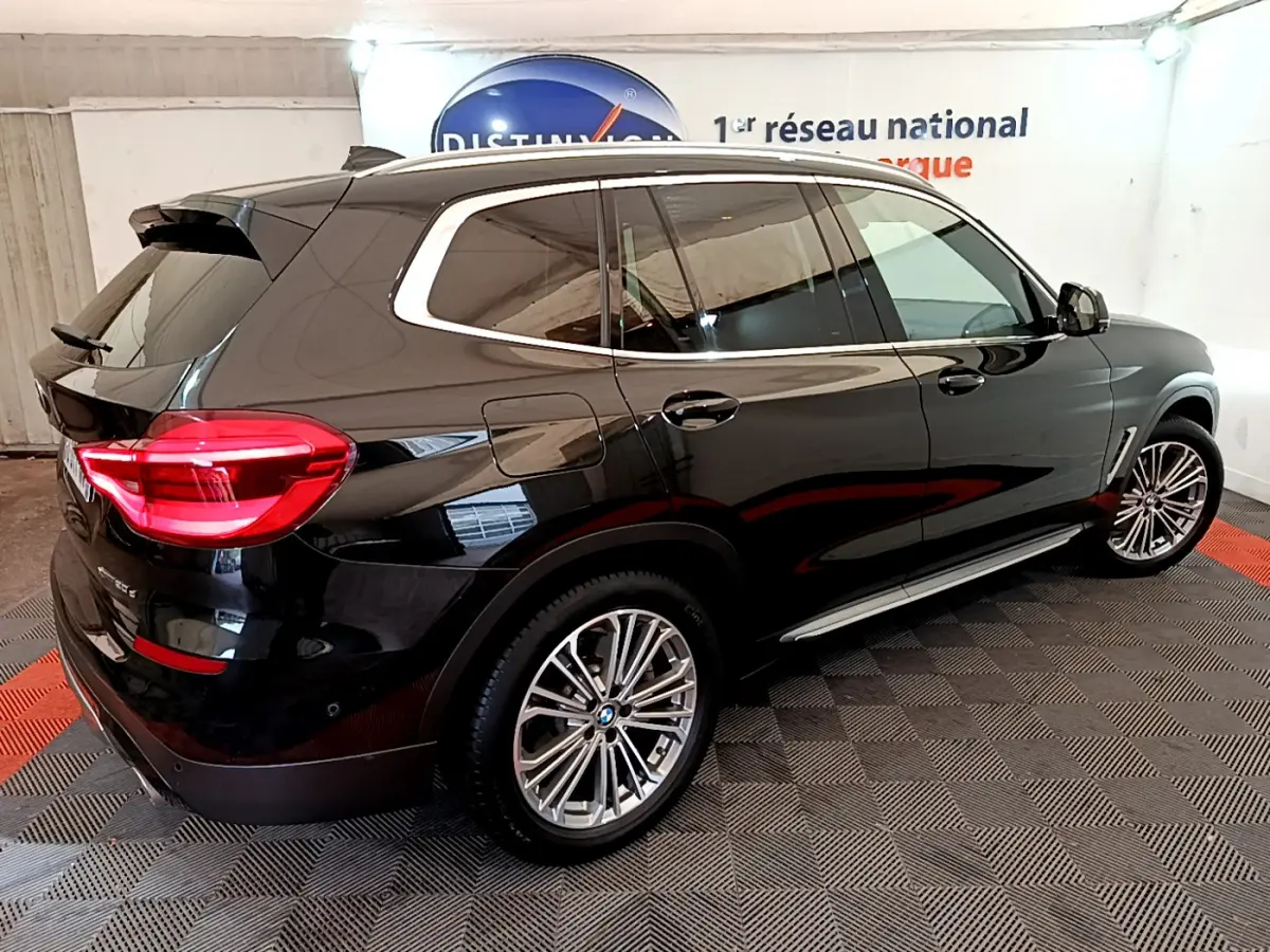BMW X3 xDrive20d noir vue 3/4 arrière côté droit, avec jantes alliage et feux arrière LED allumés.