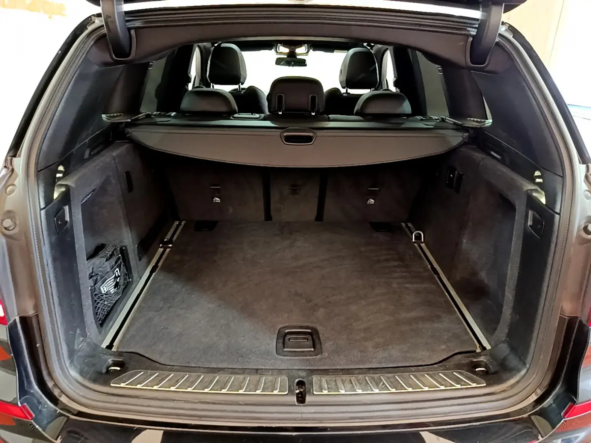 Coffre ouvert vu de l'arrière d'un BMW X3 noir, montrant un espace de chargement spacieux et tapis gris.
