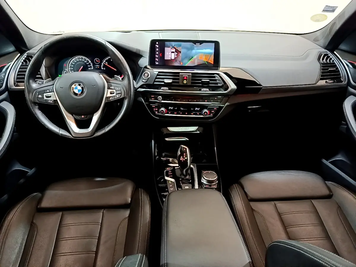 Vue intérieure avant de la BMW X3 2019, tableau de bord noir avec écran tactile et volant cuir multifonctions.