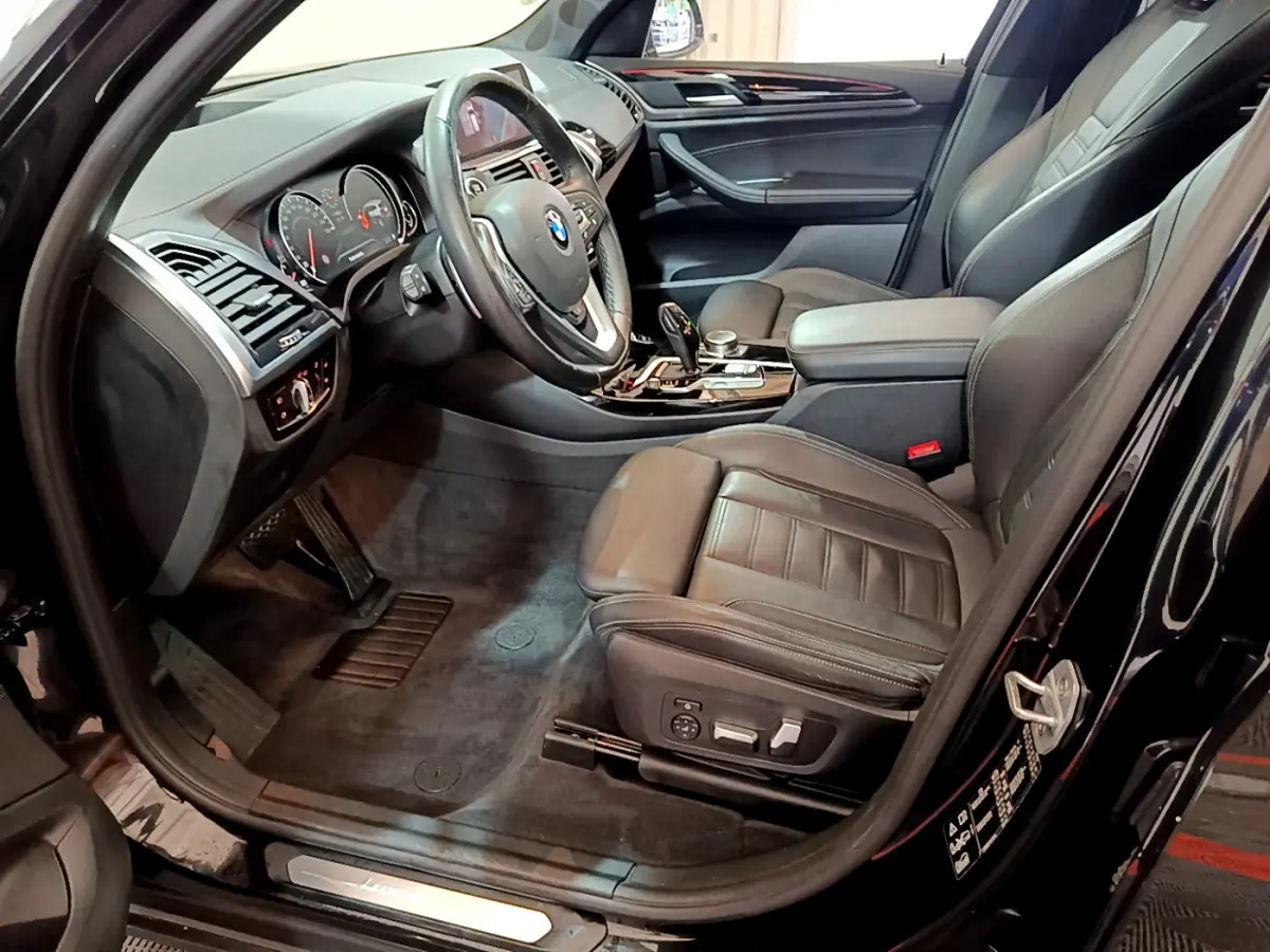 Vue intérieure côté conducteur d'une BMW X3 noire 2019, sièges cuir noirs et tableau de bord moderne avec commandes intégrées.