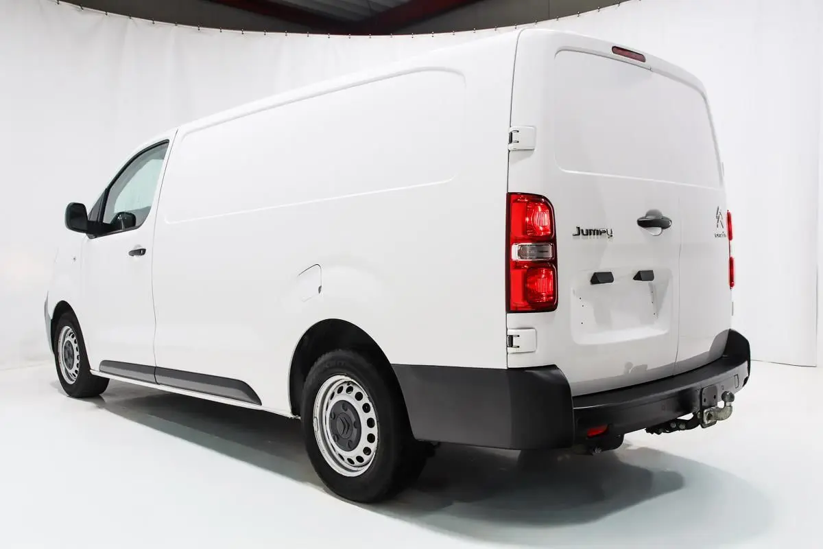 Vue 3/4 arrière droite d'un fourgon Citroën Jumpy blanc avec attelage et porte latérale coulissante.