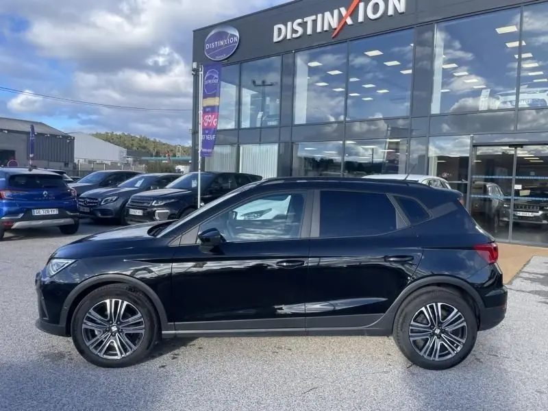 Vue latérale droite d'un SEAT Arona noir 2023 garé devant un showroom avec jantes alliage et vitres teintées.