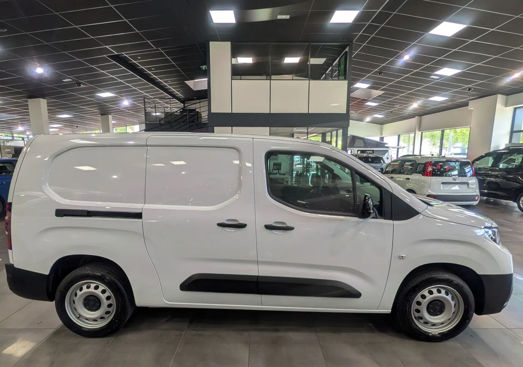 Vue de profil côté droit d’un Toyota Proace City Long blanc glacier en showroom, avec portes latérales et jantes acier.
