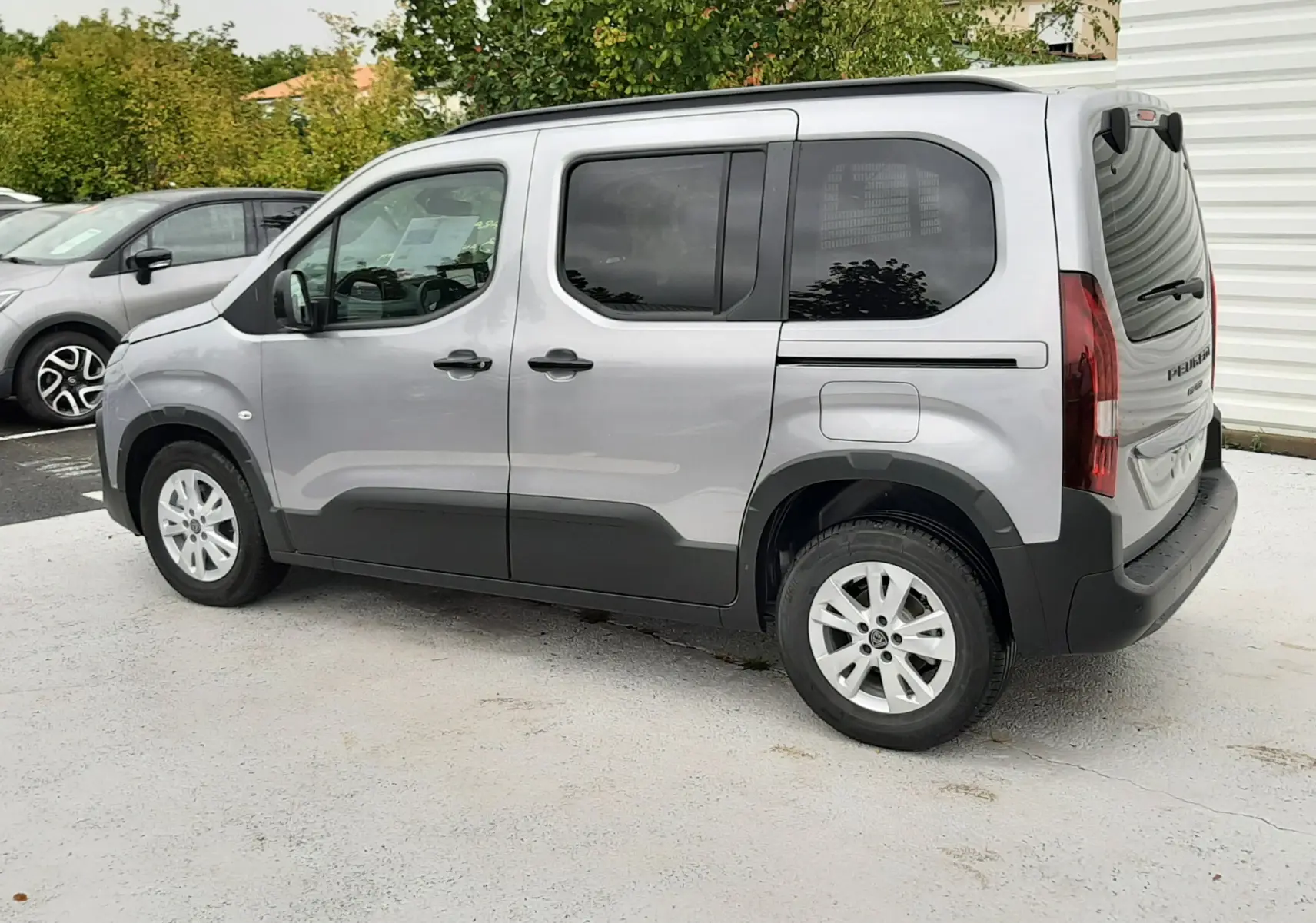 Peugeot Rifter gris acier vu de profil côté gauche, avec vitres arrière surteintées et barres de toit noires.