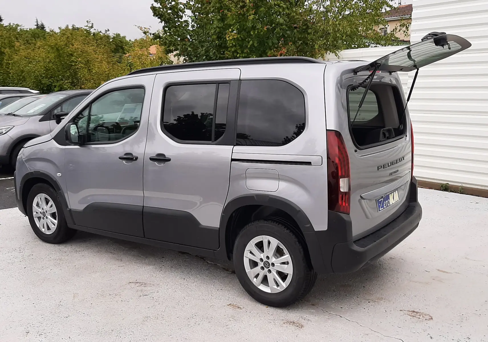 Peugeot Rifter gris acier vue 3/4 arrière droit avec lunette arrière ouverte et vitres arrière surteintées.