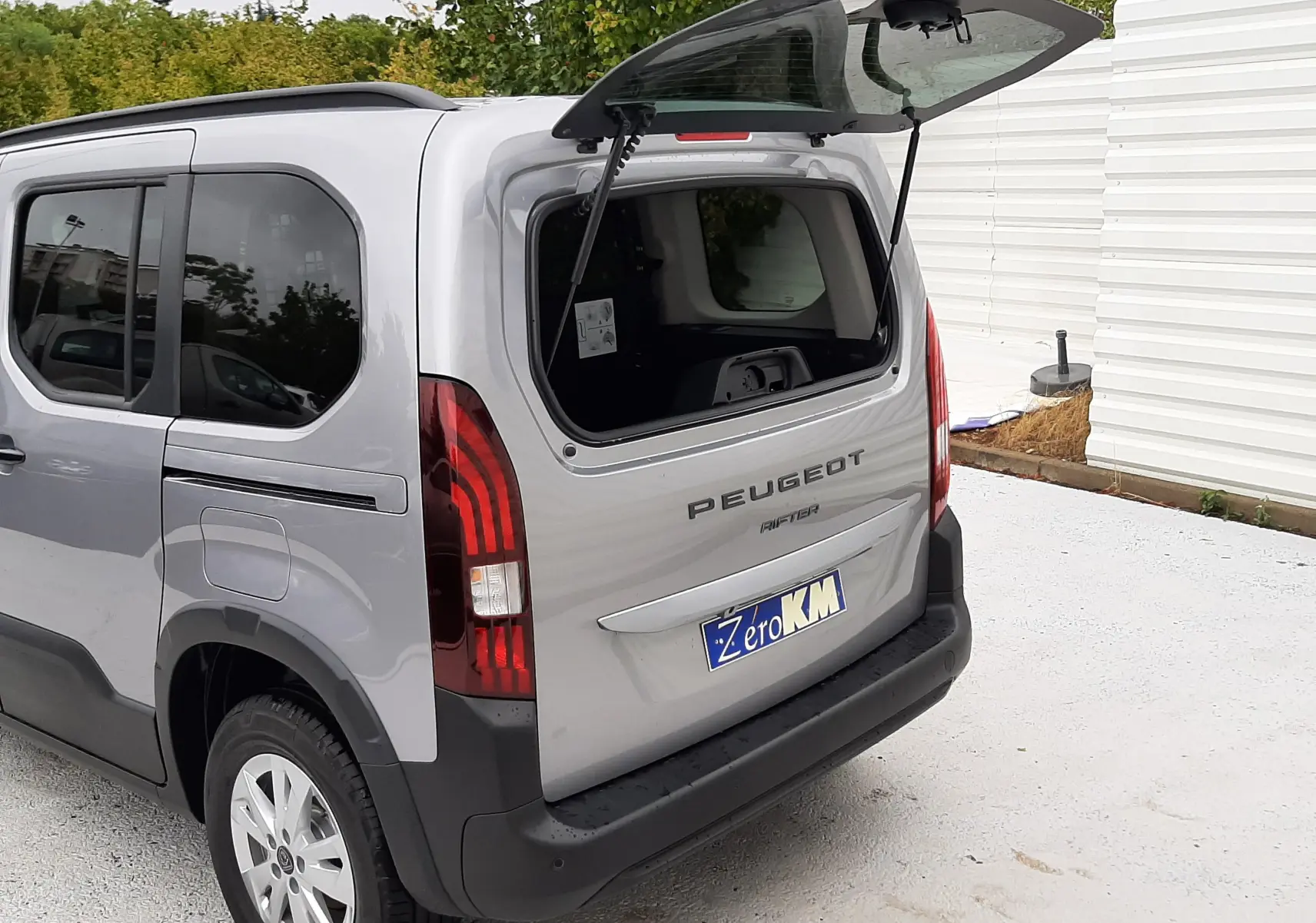 Vue 3/4 arrière droite d’un Peugeot Rifter gris acier 2026 avec hayon ouvert et vitres arrière surteintées.