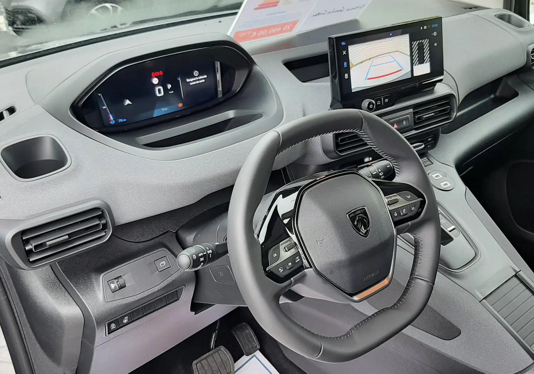 Vue intérieure côté conducteur du Peugeot Rifter gris acier 2026, avec tableau de bord numérique et écran tactile affichant la caméra de recul.