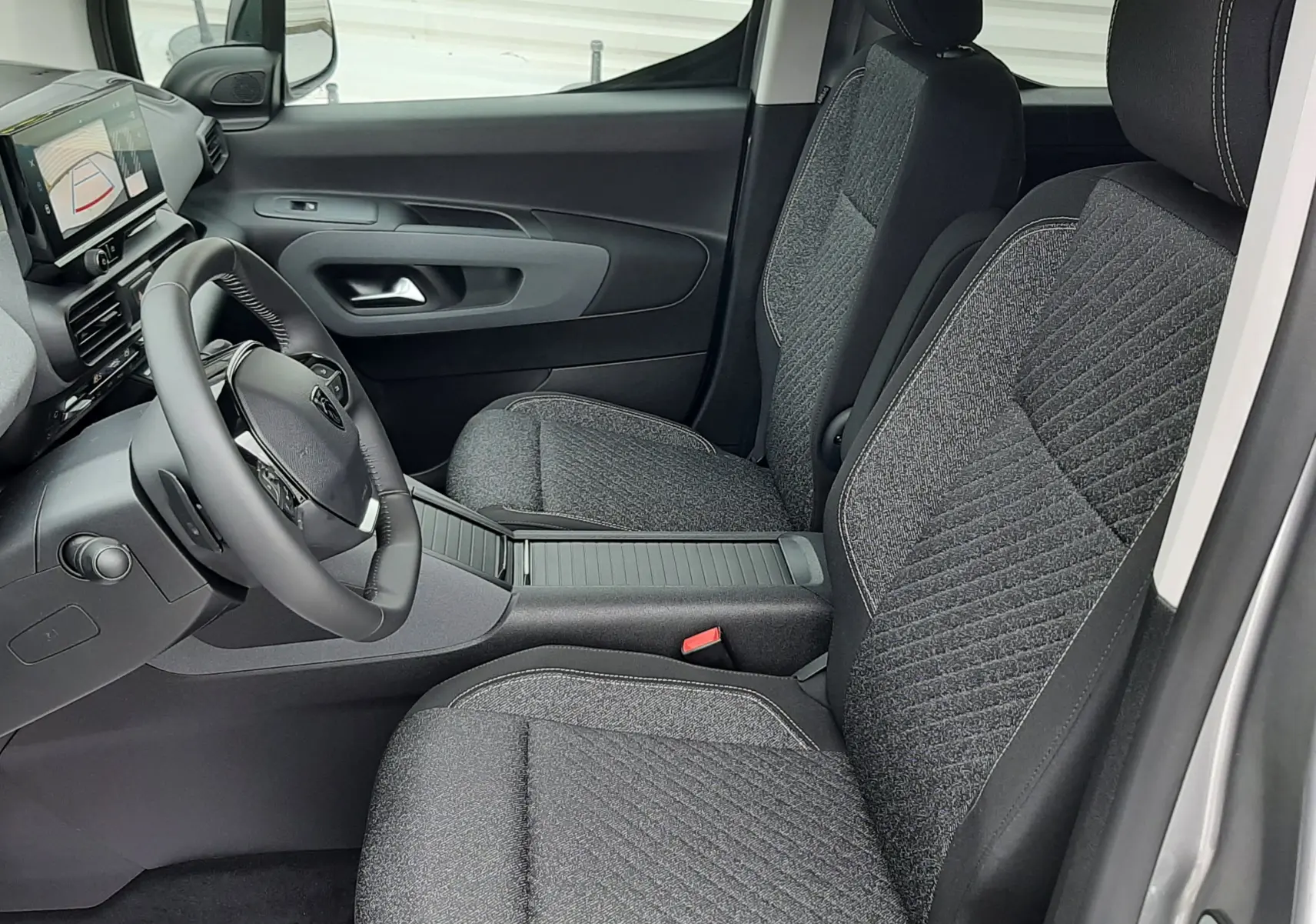 Vue intérieure côté conducteur du Peugeot Rifter 2026, sièges tissu gris, tableau de bord avec écran tactile et volant multifonction.