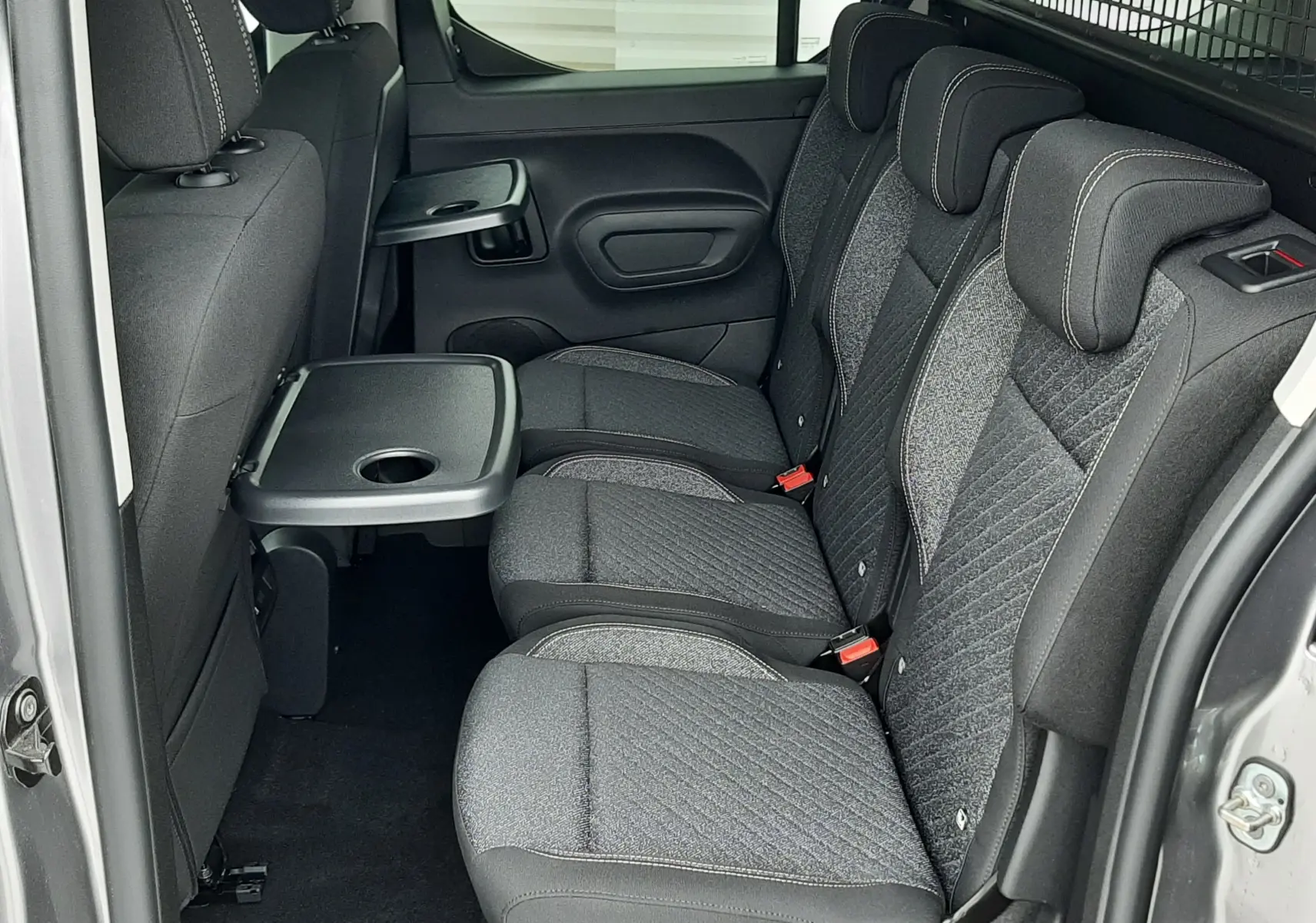 Vue latérale intérieure des sièges arrière gris tissu du Peugeot Rifter III Ph.2 avec tablette rabattable et cloison métallique.