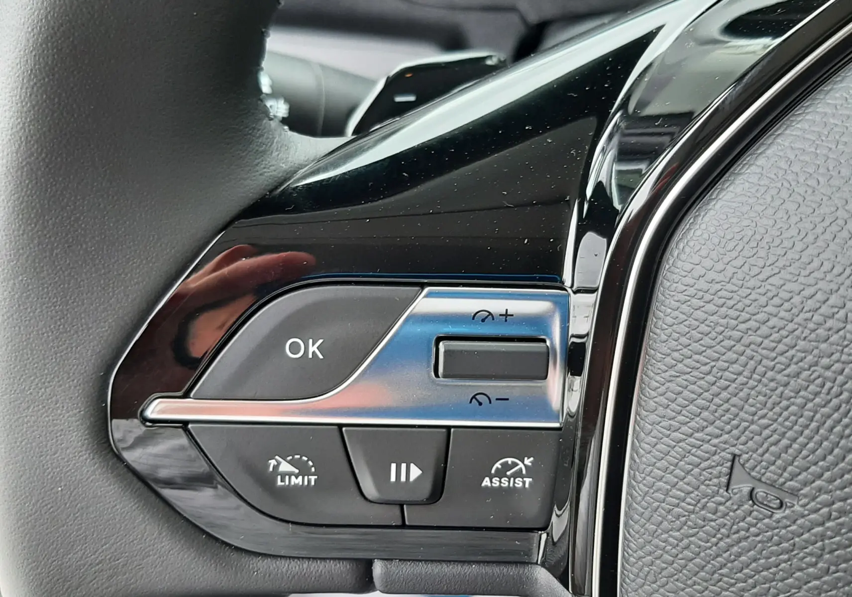Gros plan sur les commandes gauche du volant cuir noir du Peugeot Rifter gris acier, avec boutons de régulateur et limiteur.