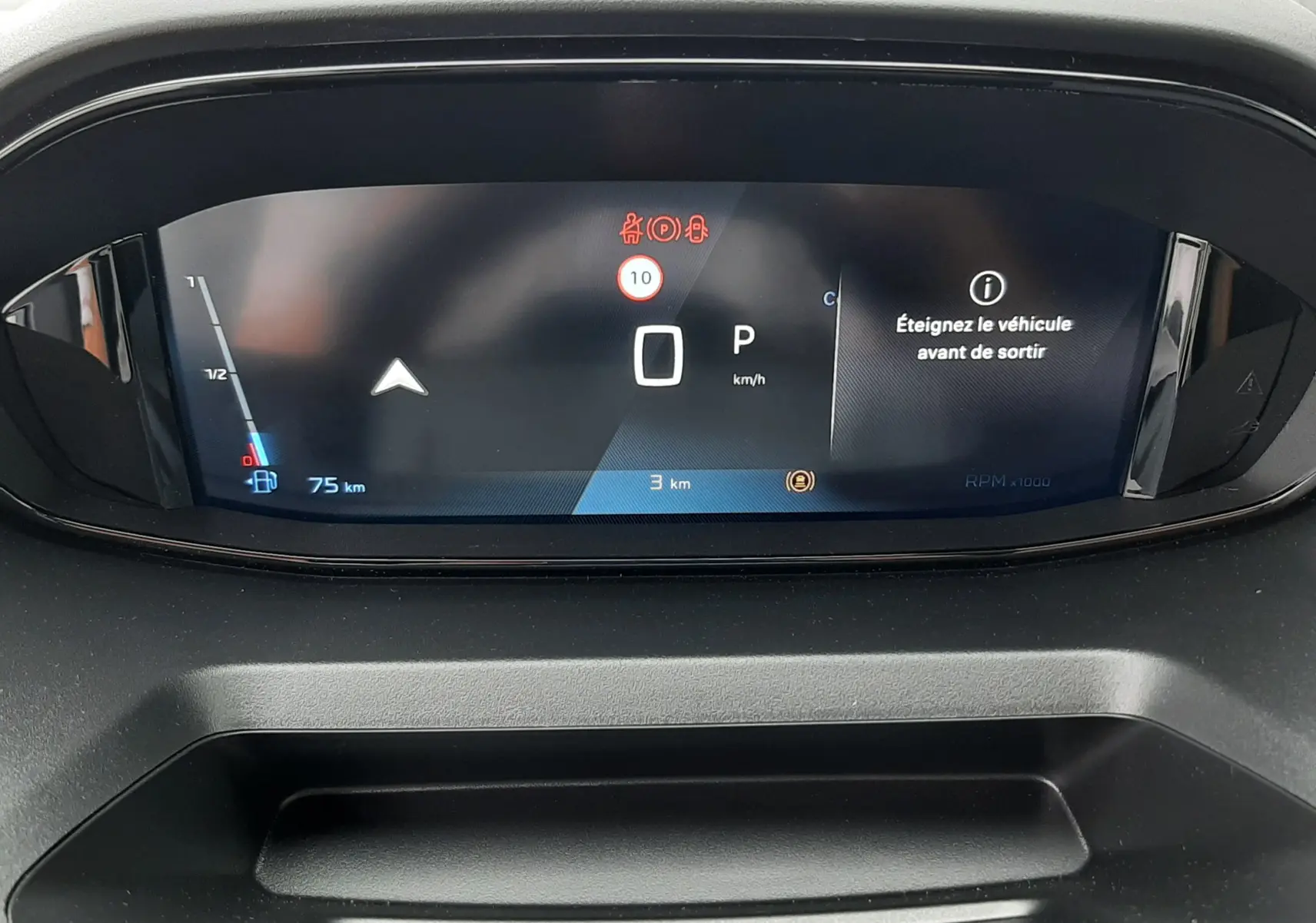 Vue rapprochée du tableau de bord numérique du Peugeot Rifter gris acier, affichant le compteur et un message d'alerte.