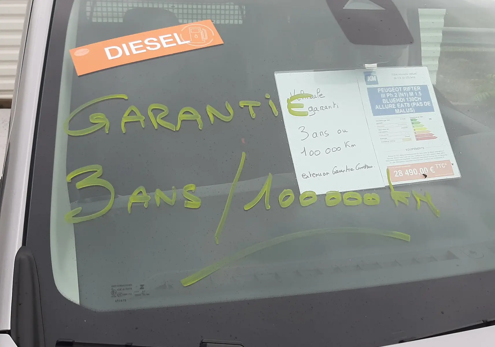 Vue avant rapprochée du Peugeot Rifter gris acier avec inscriptions de garantie et étiquette diesel sur le pare-brise.