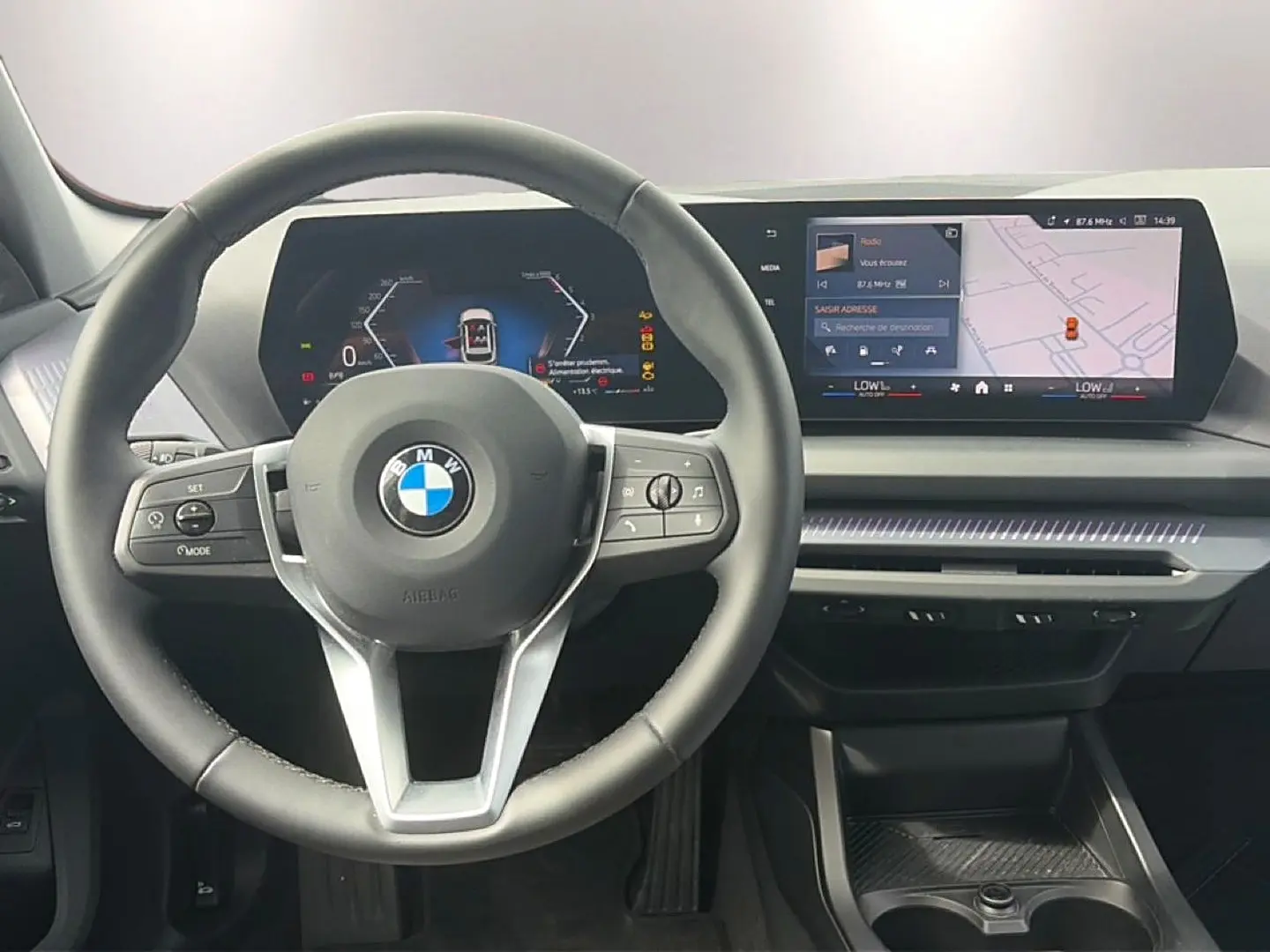 Vue intérieure centrée sur le volant cuir BMW et le tableau de bord numérique avec écran tactile panoramique.