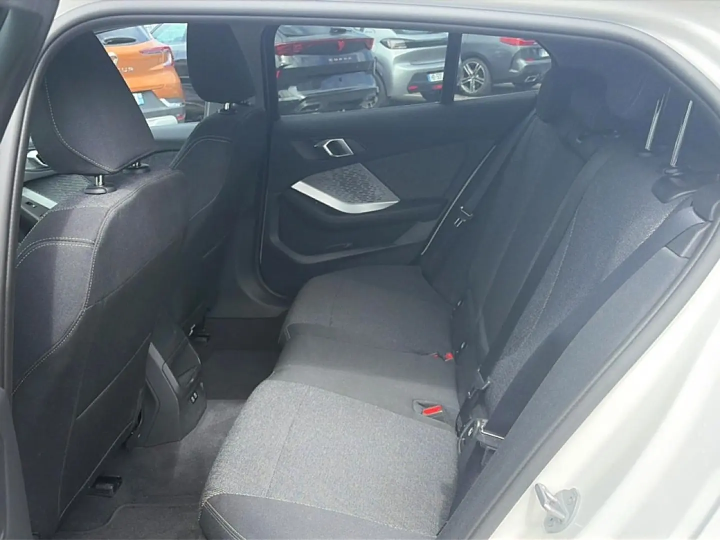 Vue intérieure arrière côté droit de la BMW Série 1 blanche, montrant la banquette tissu gris et les portes ouvertes.