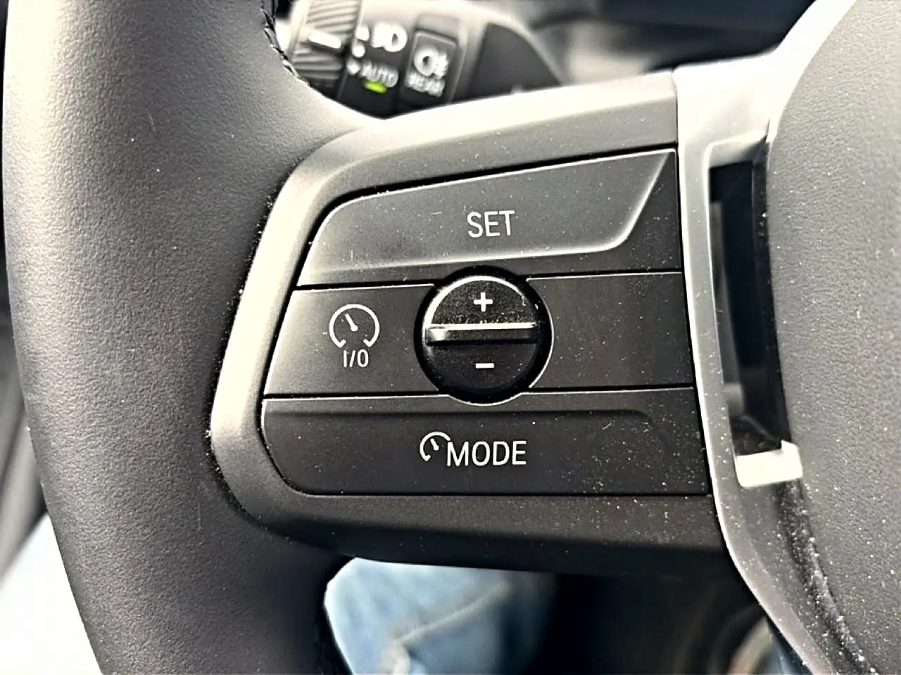 Gros plan sur les commandes de régulateur de vitesse au volant noir de la BMW Série 1 blanche 2025.