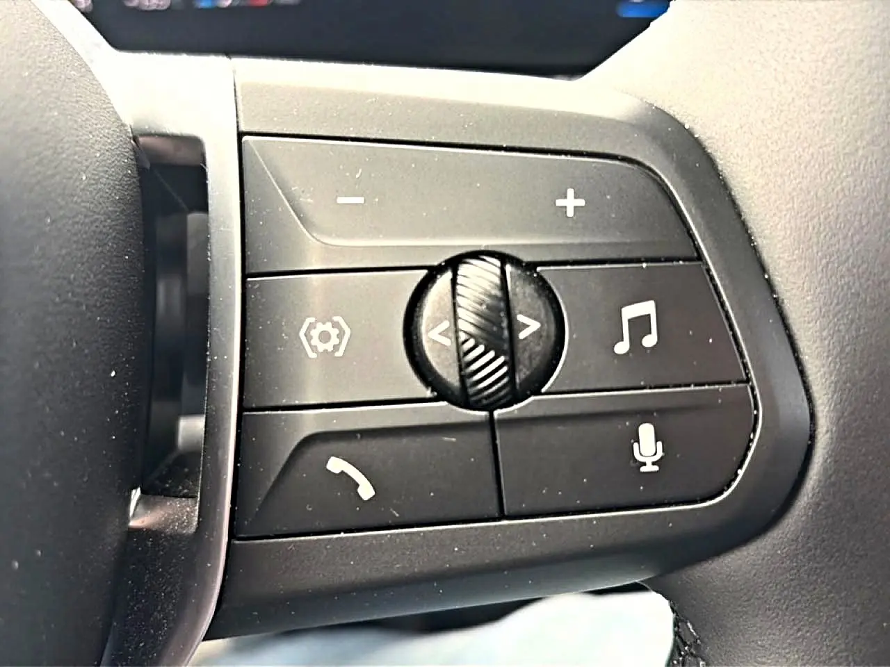 Gros plan sur les commandes noires au volant cuir de la BMW Série 1 blanche, avec boutons de volume et appel.