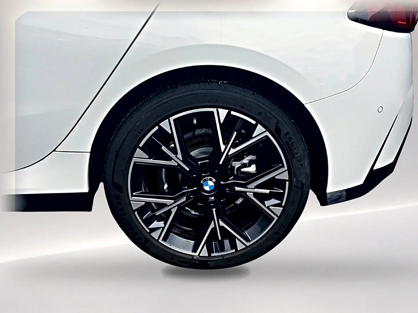 Gros plan sur la roue arrière droite noire et argentée d’une BMW Série 1 blanche pure, avec partie arrière visible.