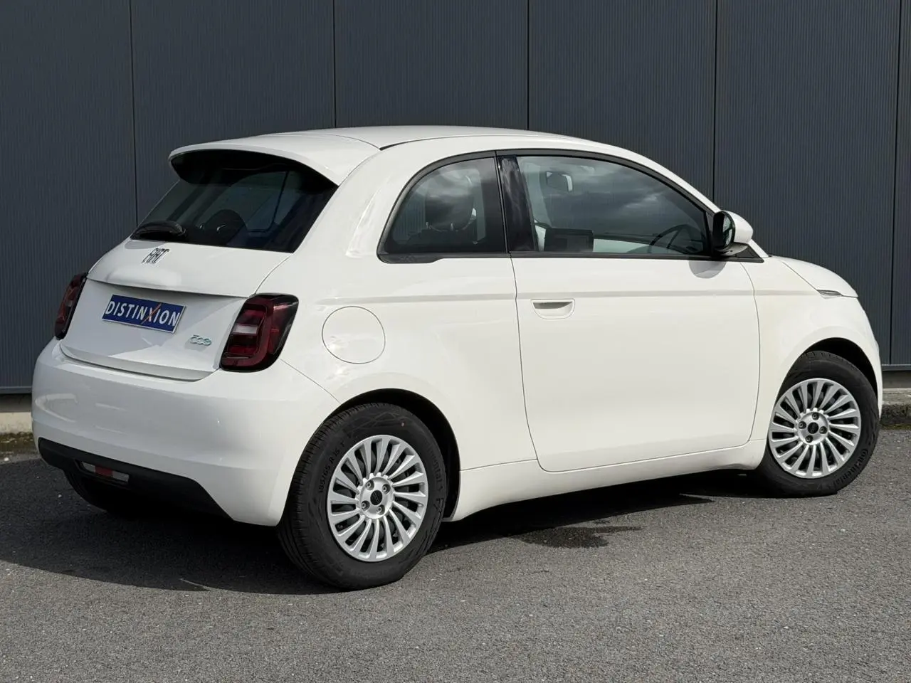 Vue 3/4 arrière droite d'une Fiat 500 électrique blanche Arctic avec jantes alu 16 pouces et feux arrière foncés.