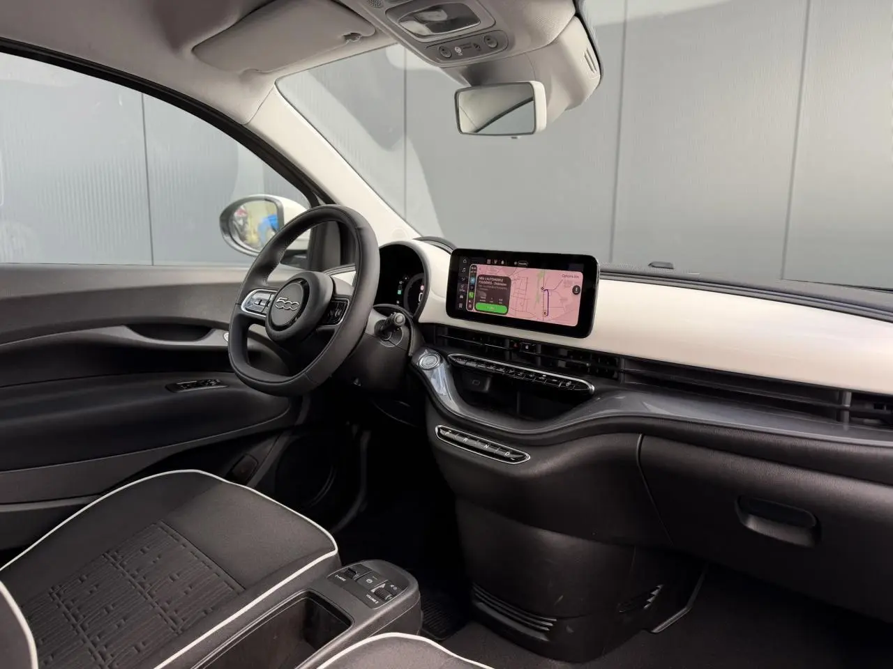 Vue intérieure côté conducteur de la Fiat 500 électrique 2024 avec tableau de bord blanc artic et écran tactile central.