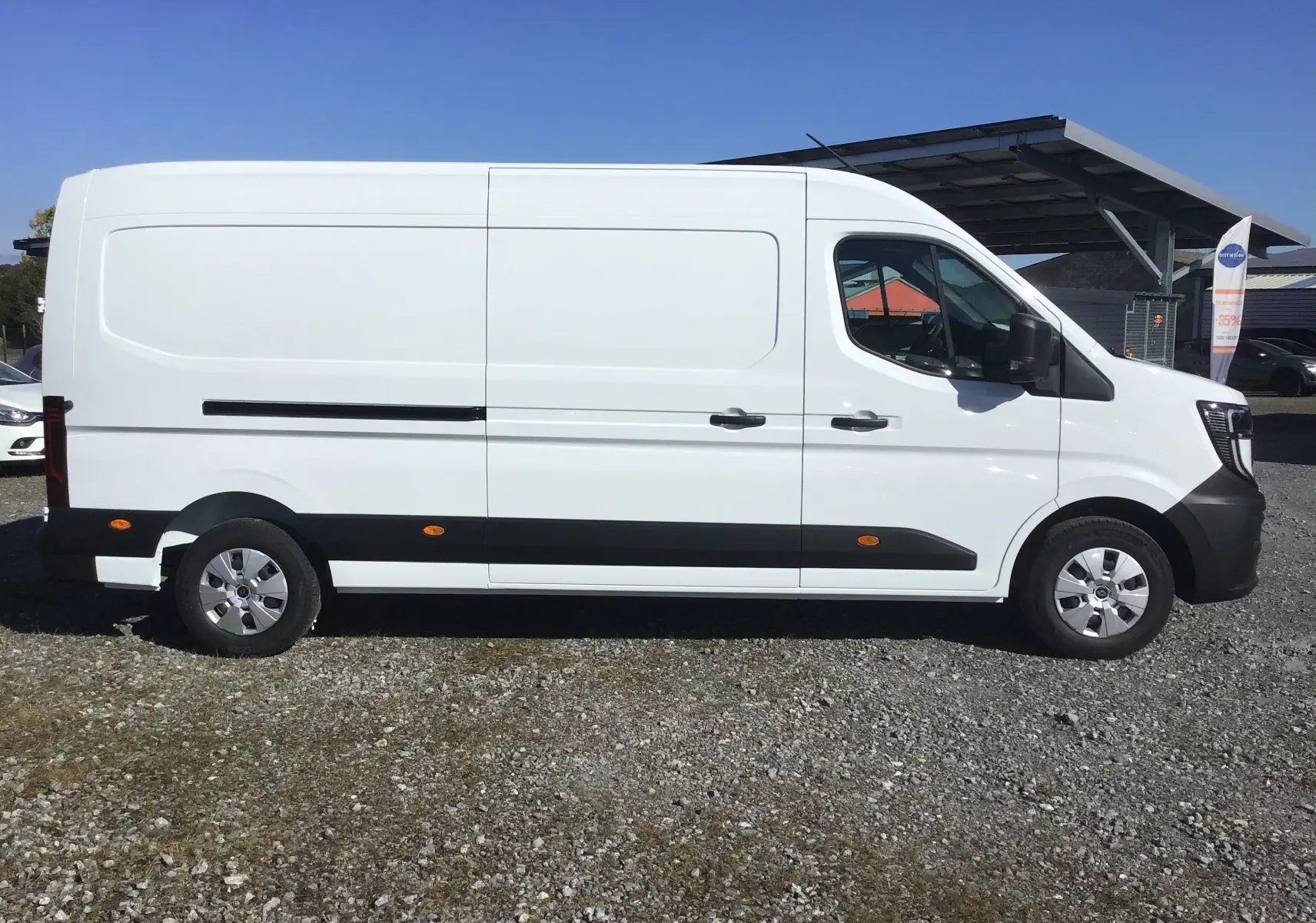 Profil droit d'un utilitaire blanc Renault Master L3H2 2025 avec bande noire et jantes argentées sur sol gravillonné.