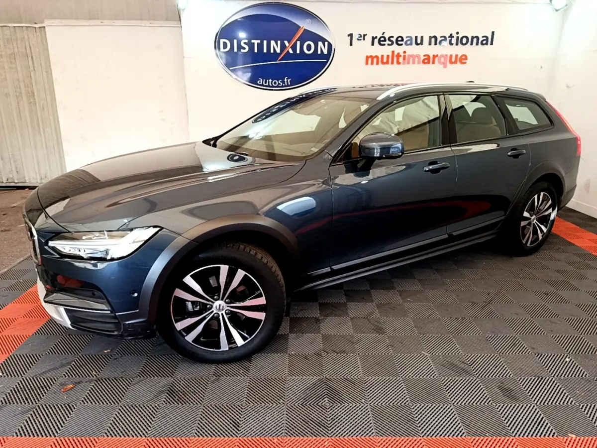 Volvo V90 Cross Country bleu en 3/4 avant droit, avec jantes alliage et rails de toit chromés visibles.