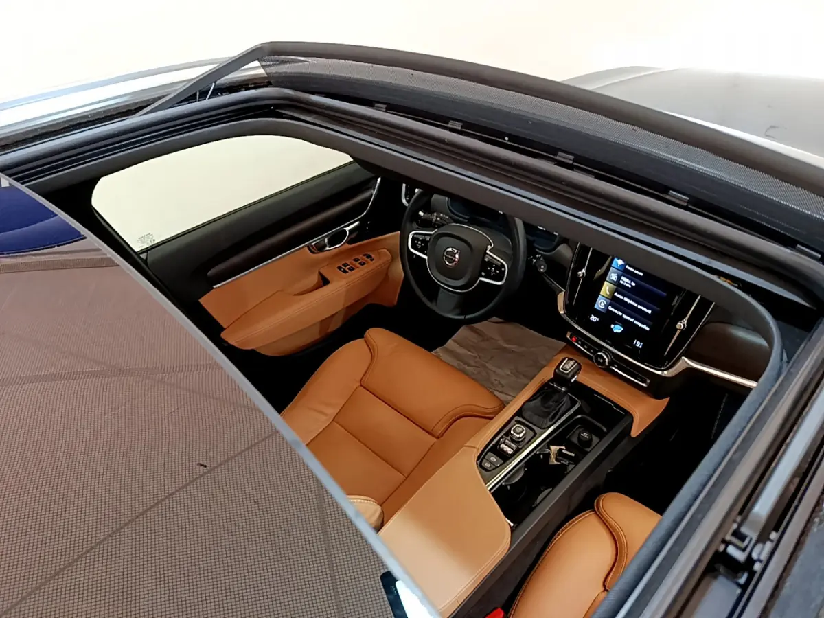 Vue intérieure par le toit ouvrant d'une Volvo V90 Cross Country 2019, sièges cuir marron et tableau de bord moderne noir.