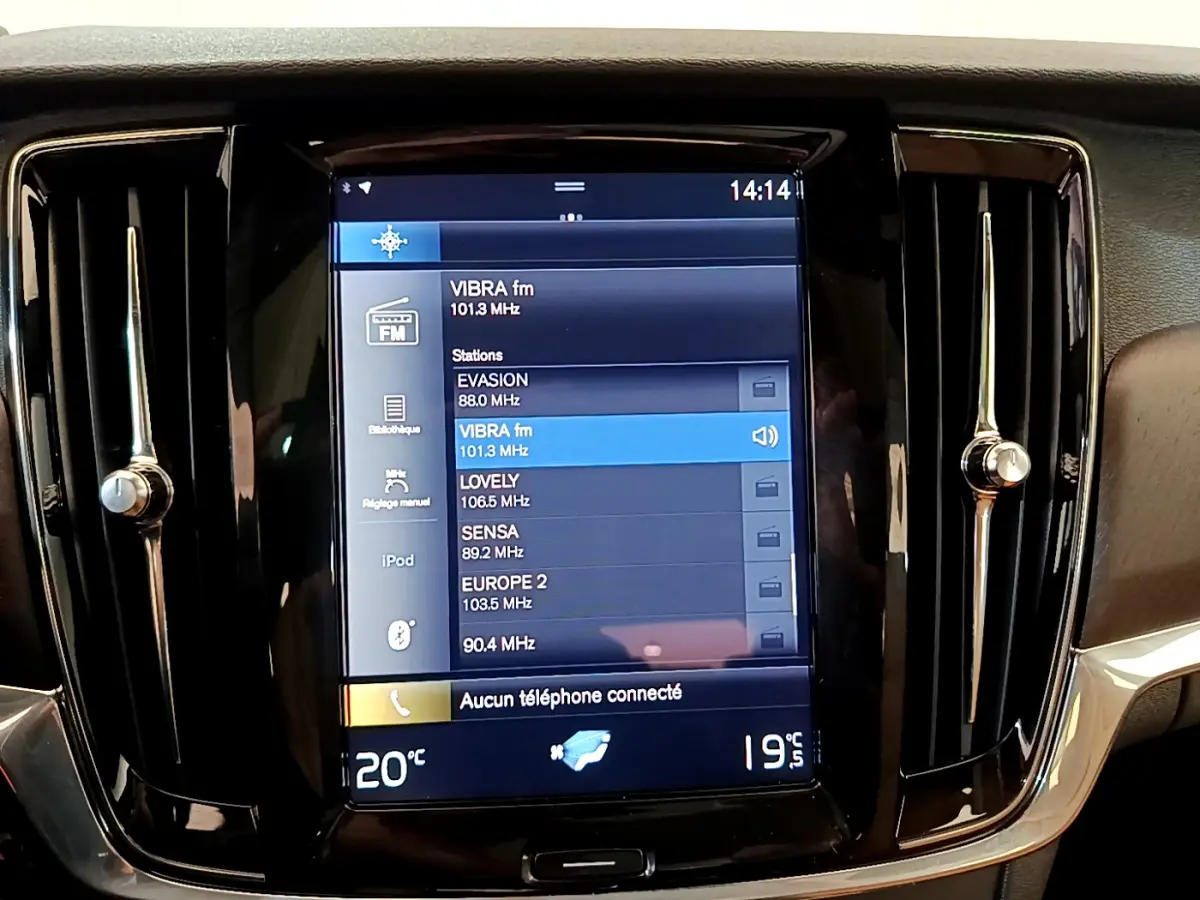 Écran tactile central noir affichant les stations radio dans l’habitacle d’un Volvo V90 Cross Country bleu.