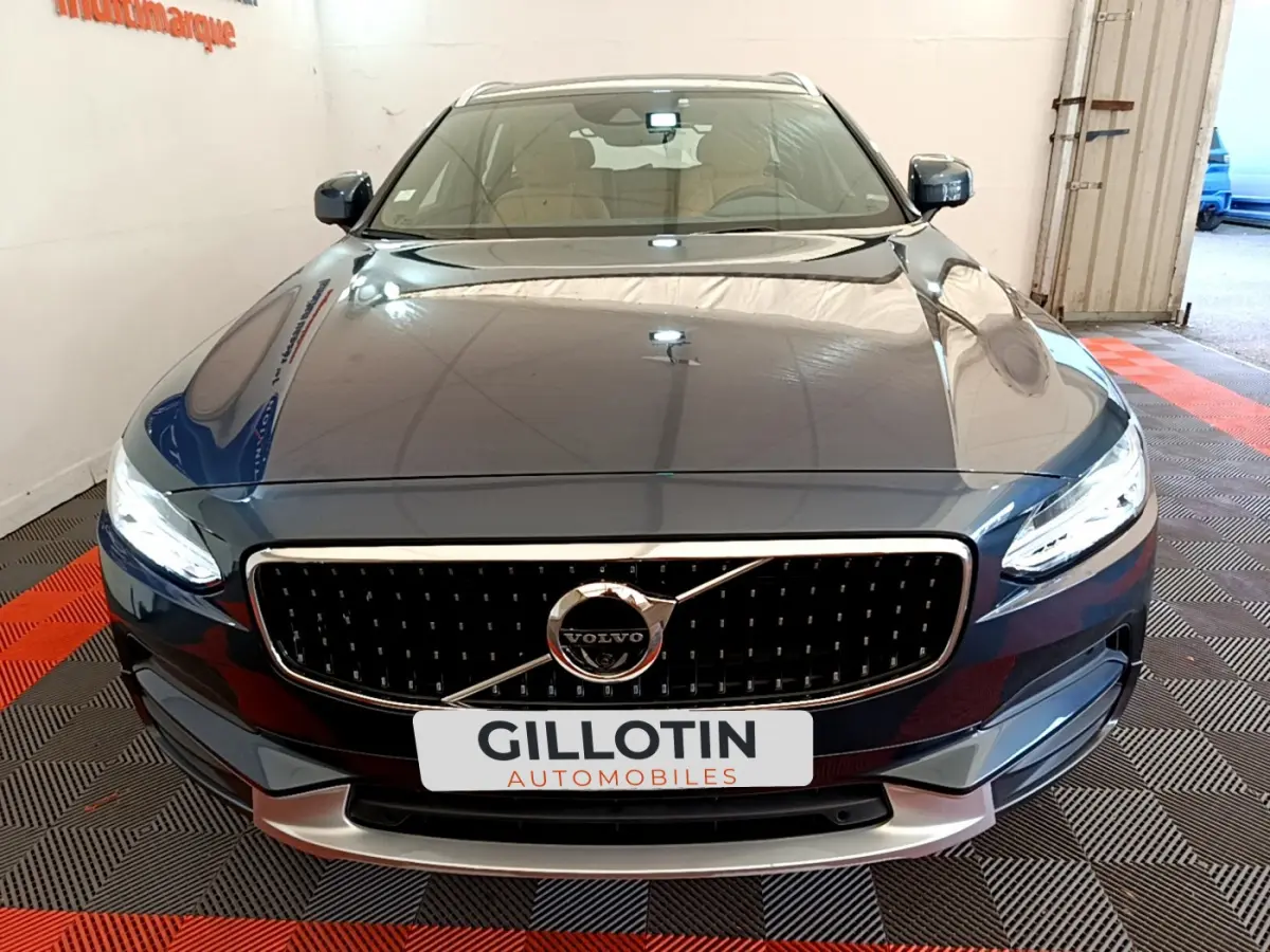 Vue avant d'un Volvo V90 Cross Country bleu avec calandre noire et phares LED allumés dans un garage.