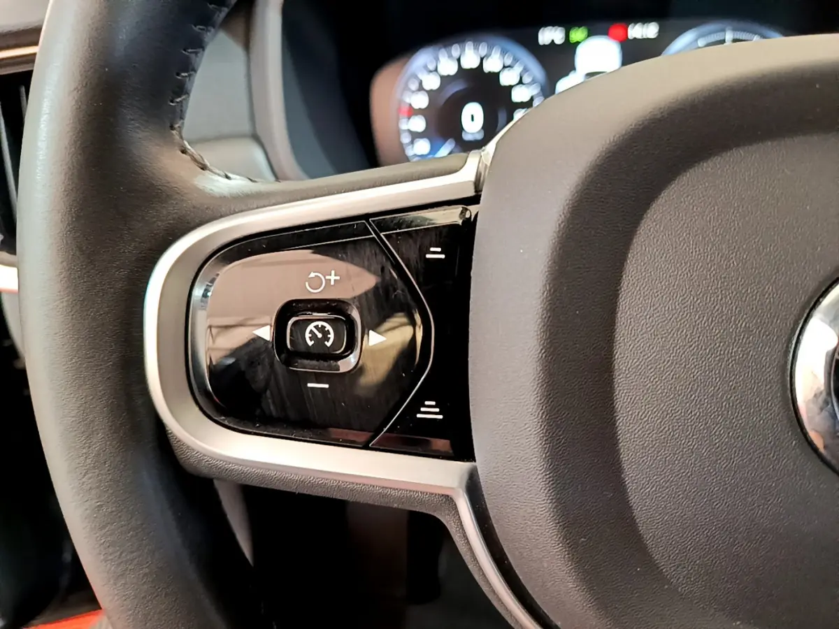 Gros plan sur les commandes gauche du volant noir du Volvo V90 Cross Country 2019 avec tableau de bord numérique en arrière-plan.