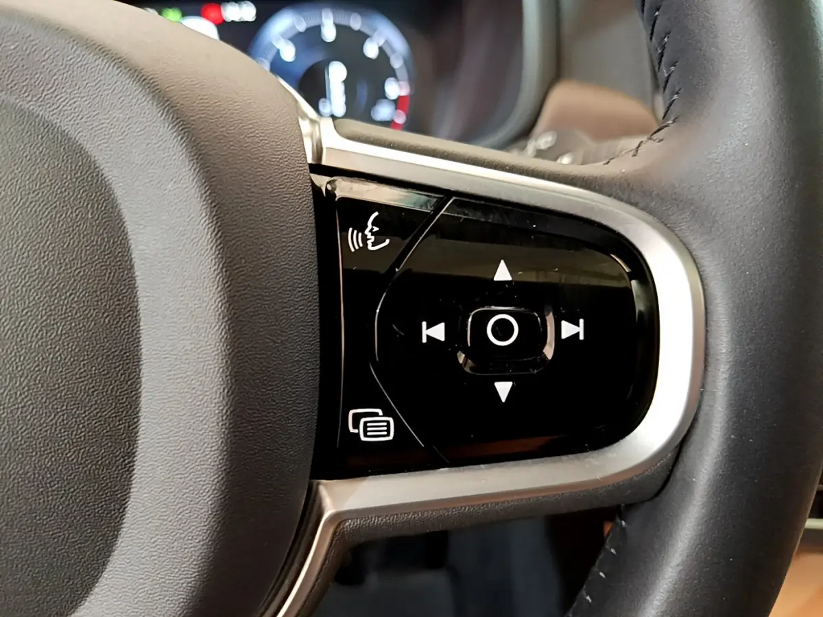 Gros plan sur les commandes vocales et de navigation intégrées au volant en cuir noir du Volvo V90 Cross Country.