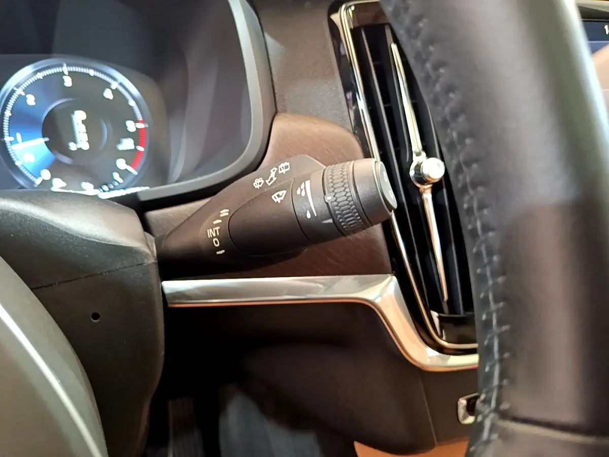 Gros plan sur la manette d’essuie-glace côté gauche du tableau de bord bois et chrome du Volvo V90 Cross Country bleu 2019.