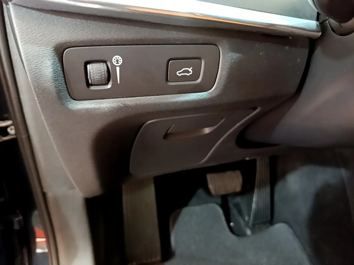 Gros plan sur les commandes sous le tableau de bord côté conducteur du Volvo V90 Cross Country bleu, bouton ouverture coffre visible.