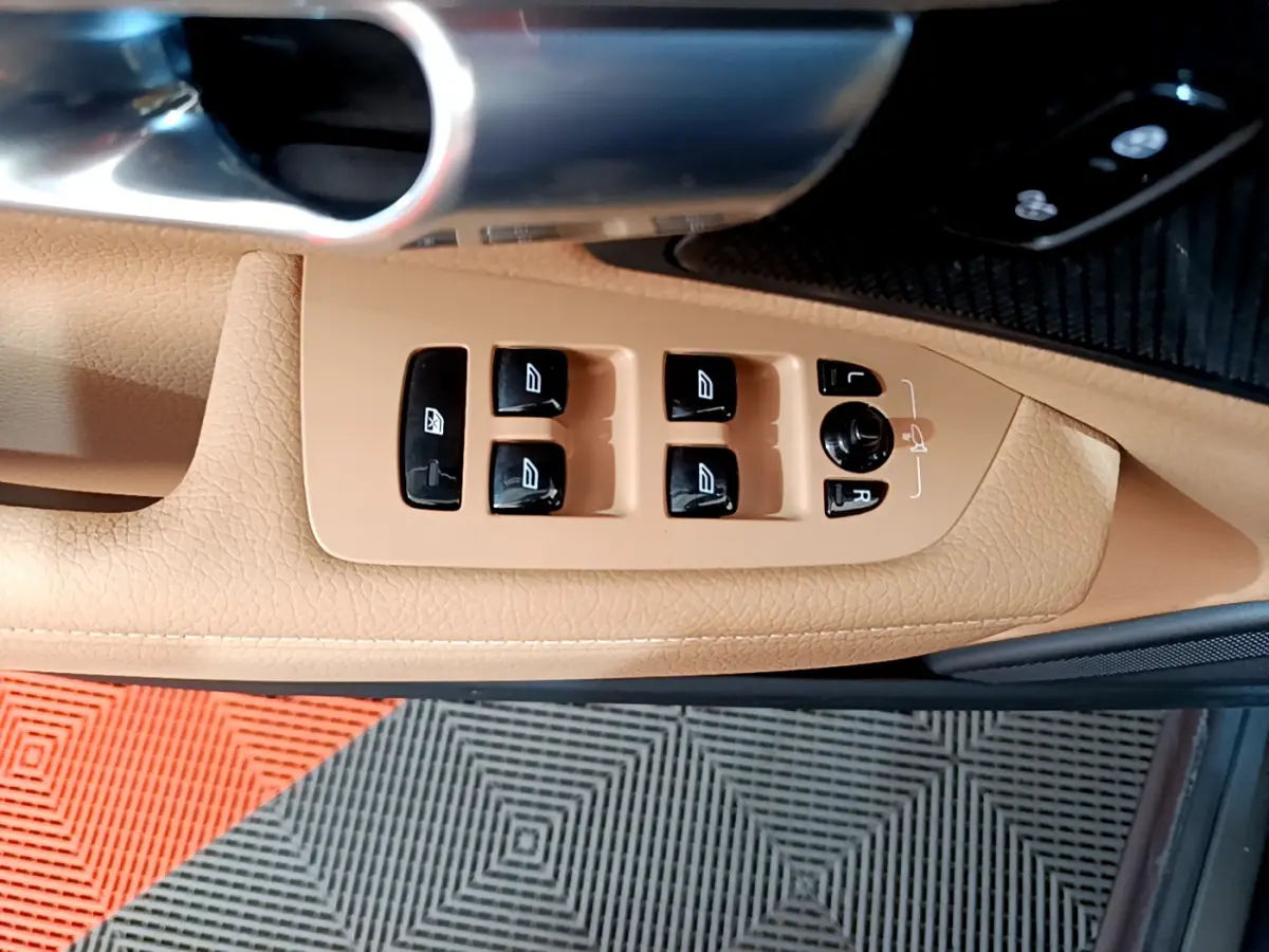 Gros plan sur les commandes des vitres et rétroviseurs sur la porte beige côté conducteur d’un Volvo V90 Cross Country.