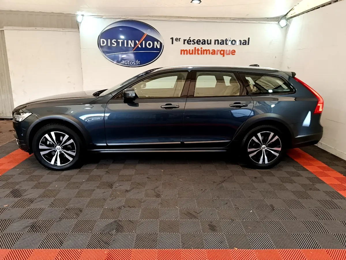 Vue de profil côté gauche d’un Volvo V90 Cross Country bleu dans un showroom avec sol à damier noir et rouge.