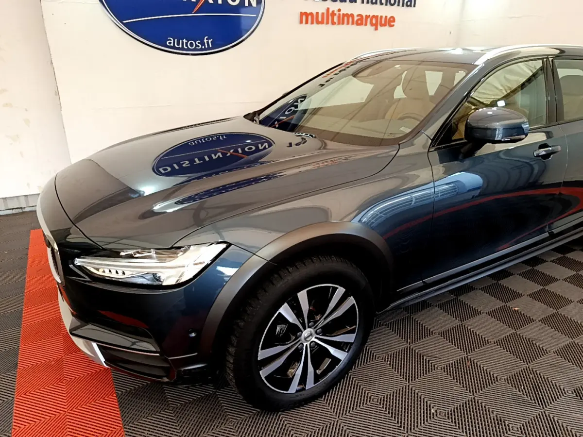 Vue 3/4 avant droit d'un Volvo V90 Cross Country bleu métallisé avec jantes alliage et phares LED allumés.