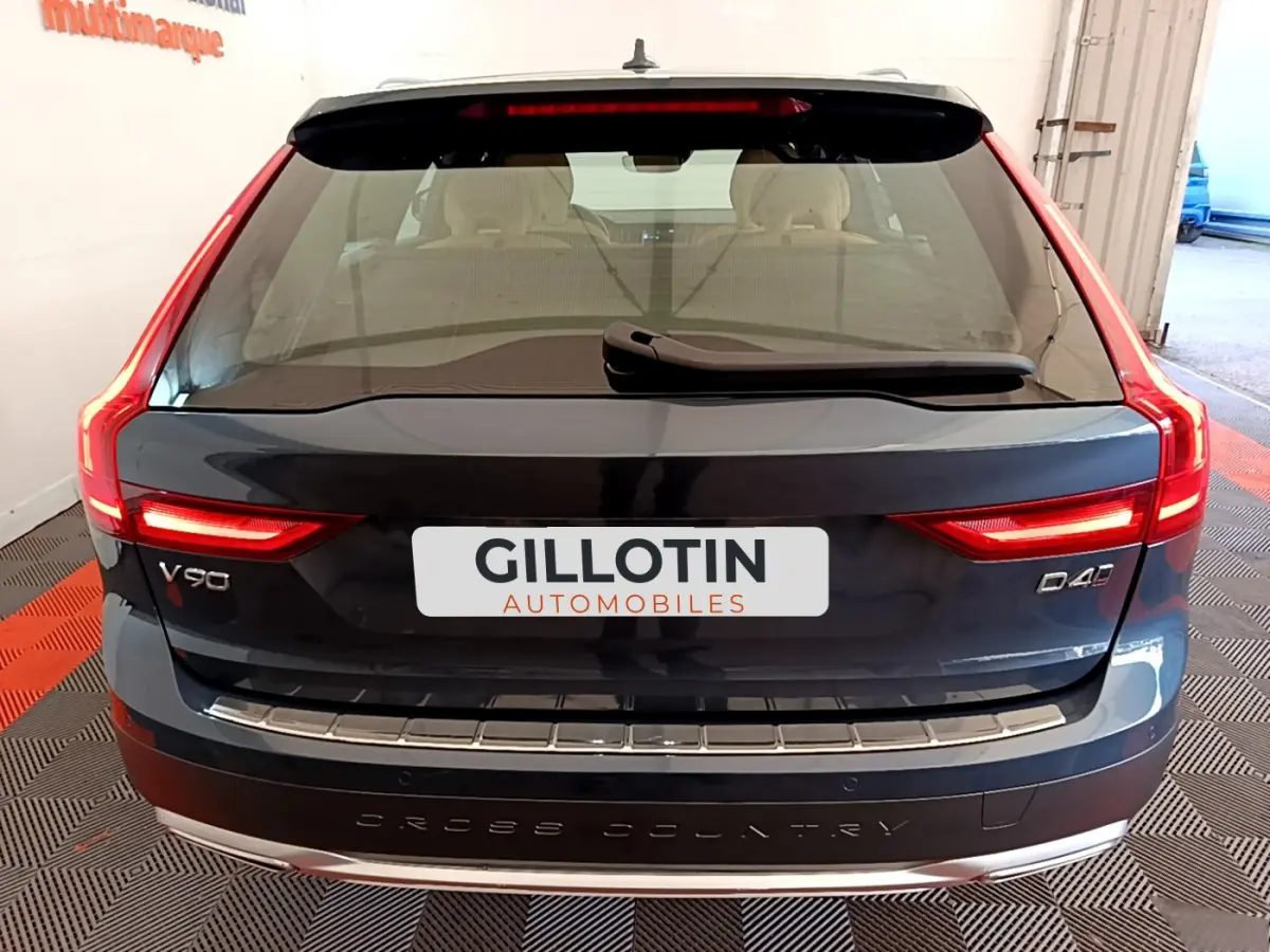 Vue arrière d'un Volvo V90 Cross Country bleu foncé avec feux LED allumés et badge D4 sur un sol à damier.
