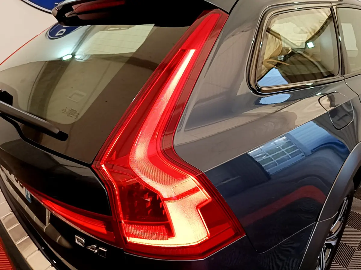 Vue arrière côté droit d'un Volvo V90 Cross Country bleu avec feux arrière LED allumés dans un garage.