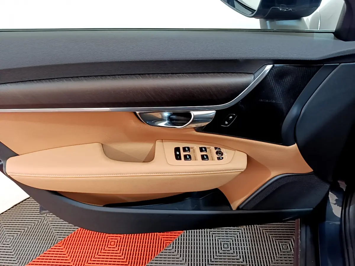 Vue intérieure côté conducteur de la porte beige et noire du Volvo V90 Cross Country bleu avec commandes de vitres et poignée chrome.