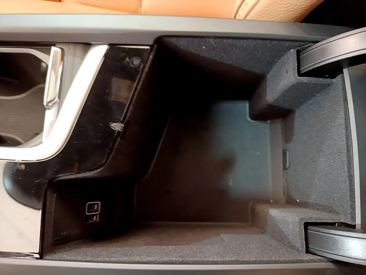 Vue en plongée du rangement central intérieur noir du Volvo V90 Cross Country avec prise USB visible.