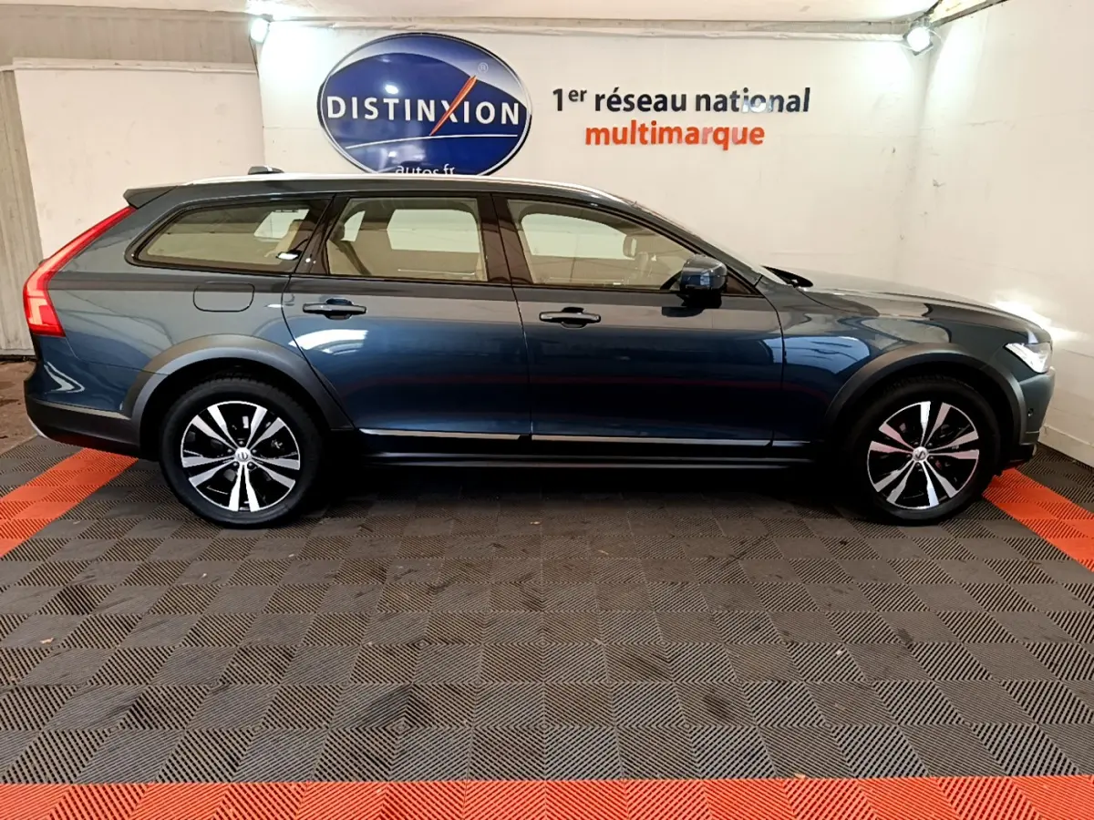 Profil côté gauche d'un Volvo V90 Cross Country bleu 2019, avec jantes noires et toit noir contrasté en intérieur showroom.