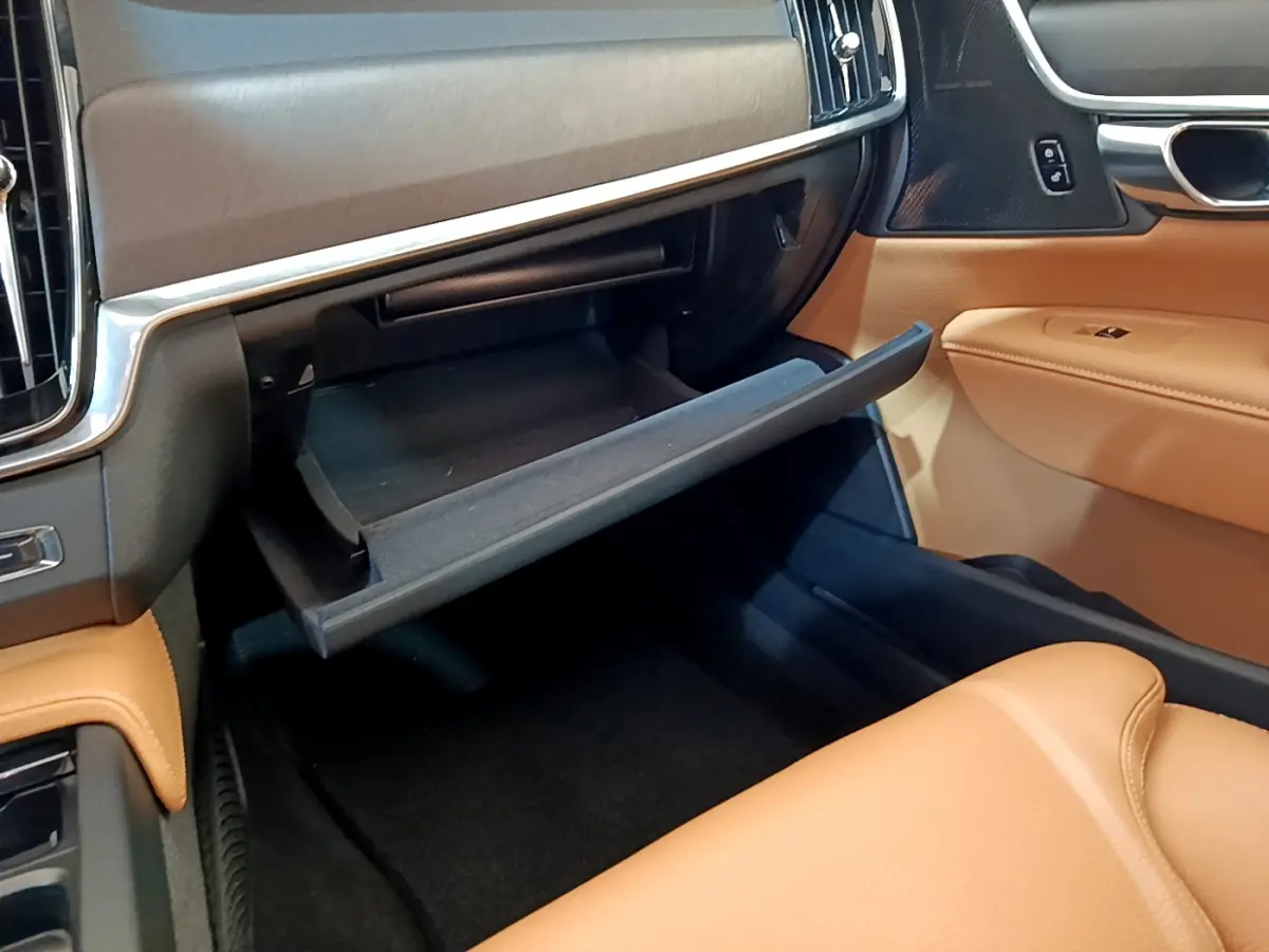 Gros plan sur la boîte à gants ouverte côté passager, intérieur cuir beige et tableau de bord noir du Volvo V90 Cross Country.