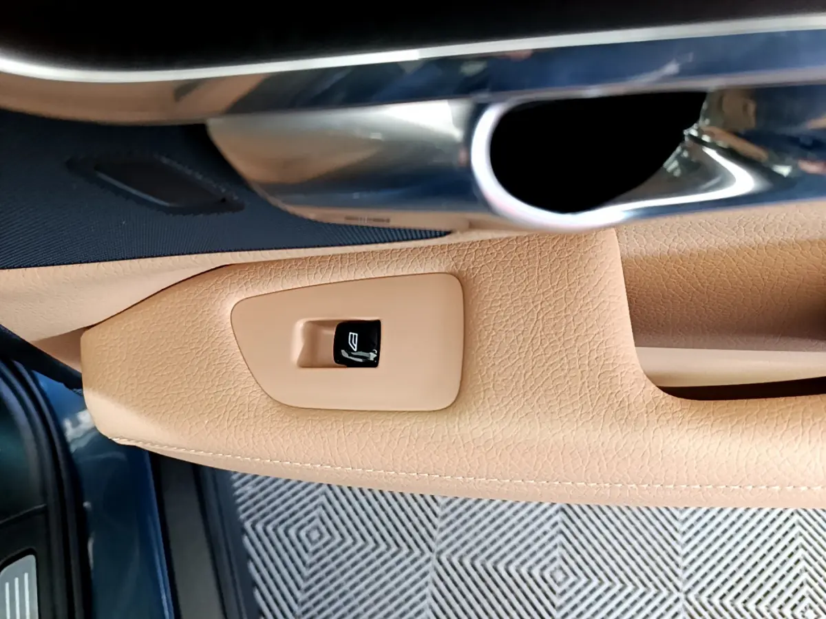 Détail de la poignée intérieure côté gauche en cuir beige avec bouton de fermeture sur Volvo V90 Cross Country bleu.