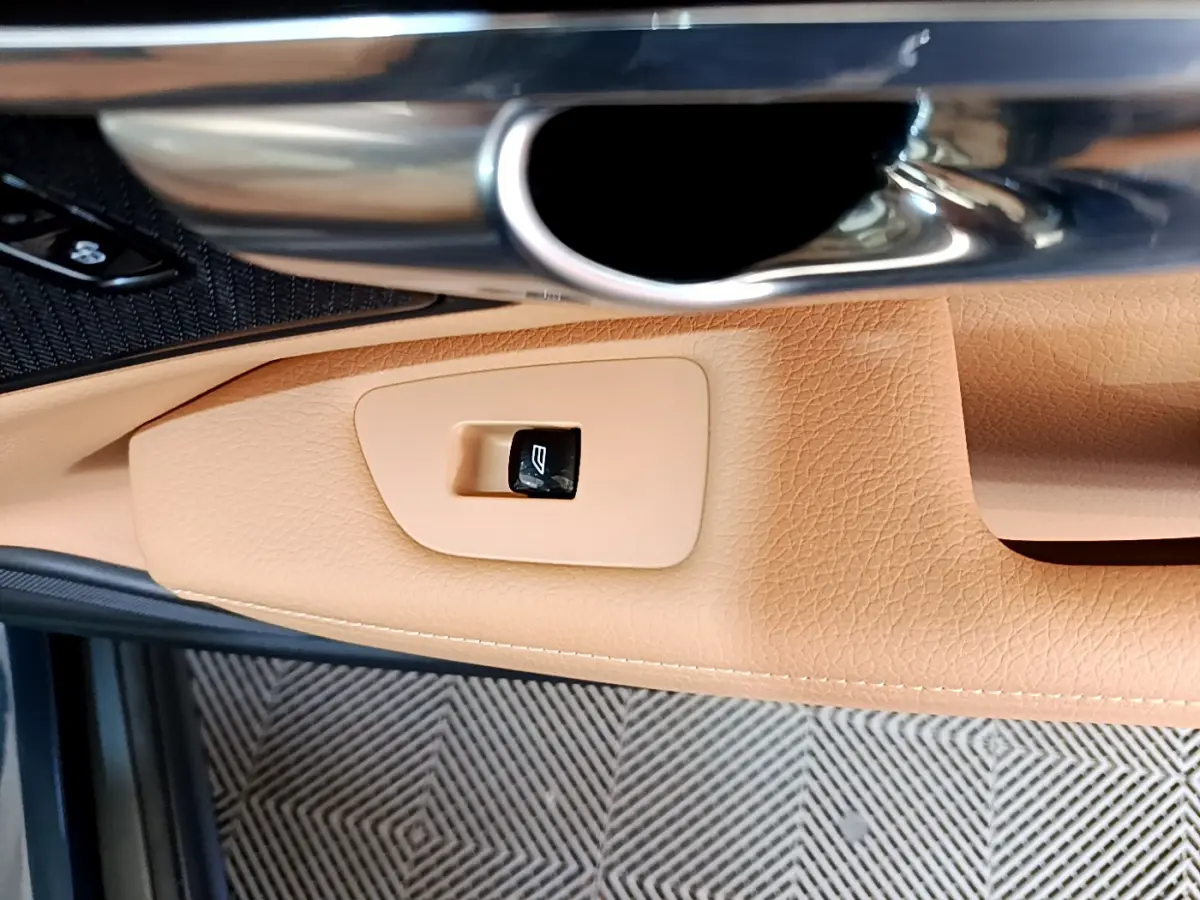 Détail de la poignée intérieure et bouton de lève-vitre en cuir beige du côté gauche d’une Volvo V90 Cross Country bleu.